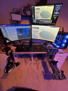 Multi-monitor flight simulator gaming setup with flight controls, microphone, illuminated PC tower and several screens displaying flight simulation software.