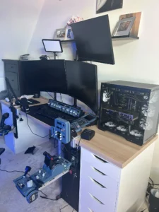 Home flight simulator setup with three monitors, flight control panels, throttle and joystick controls, microphone, keyboard and a custom-built PC.