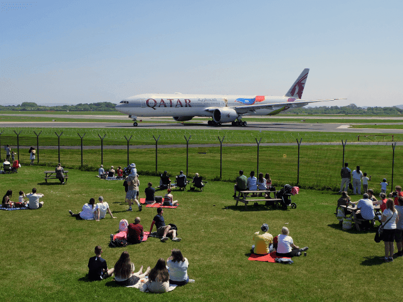 Plane spotters watching a Qatar Airways aircraft from Manchester Airport Runway Viewing Park.